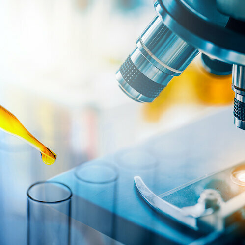 Dropping yellow liquid sample to test tube with microscope. Medical, pharmaceutical and scientific research and development concept.